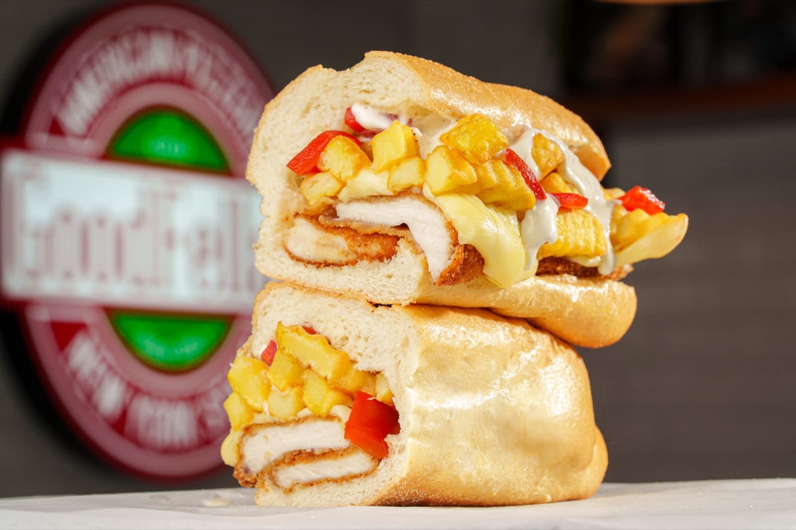 Sandwich au poulet pané, frites et sauce, devant le logo GoodFellas